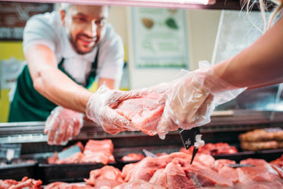 Person selecting meat at a butcher shop with a worker in the background.