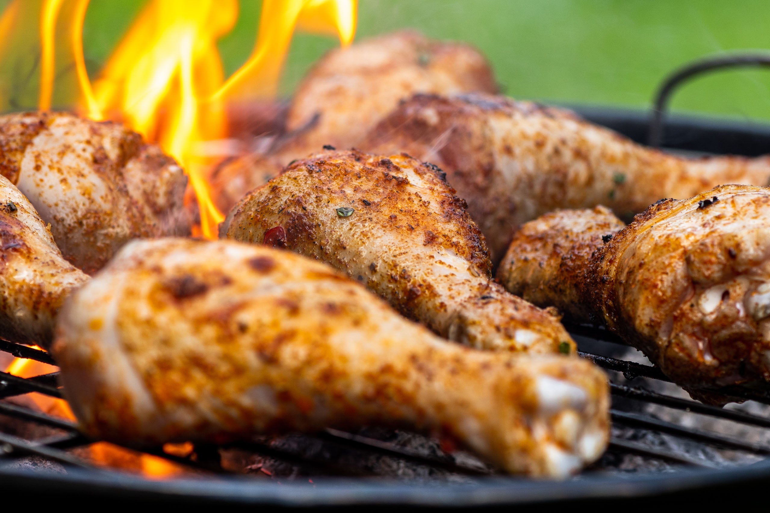Grilled chicken drumsticks on a barbecue grill with flames.