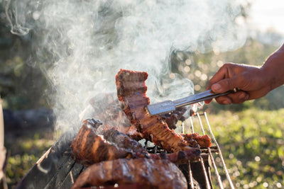 Person grilling ribs over an open flame with smoke in the background