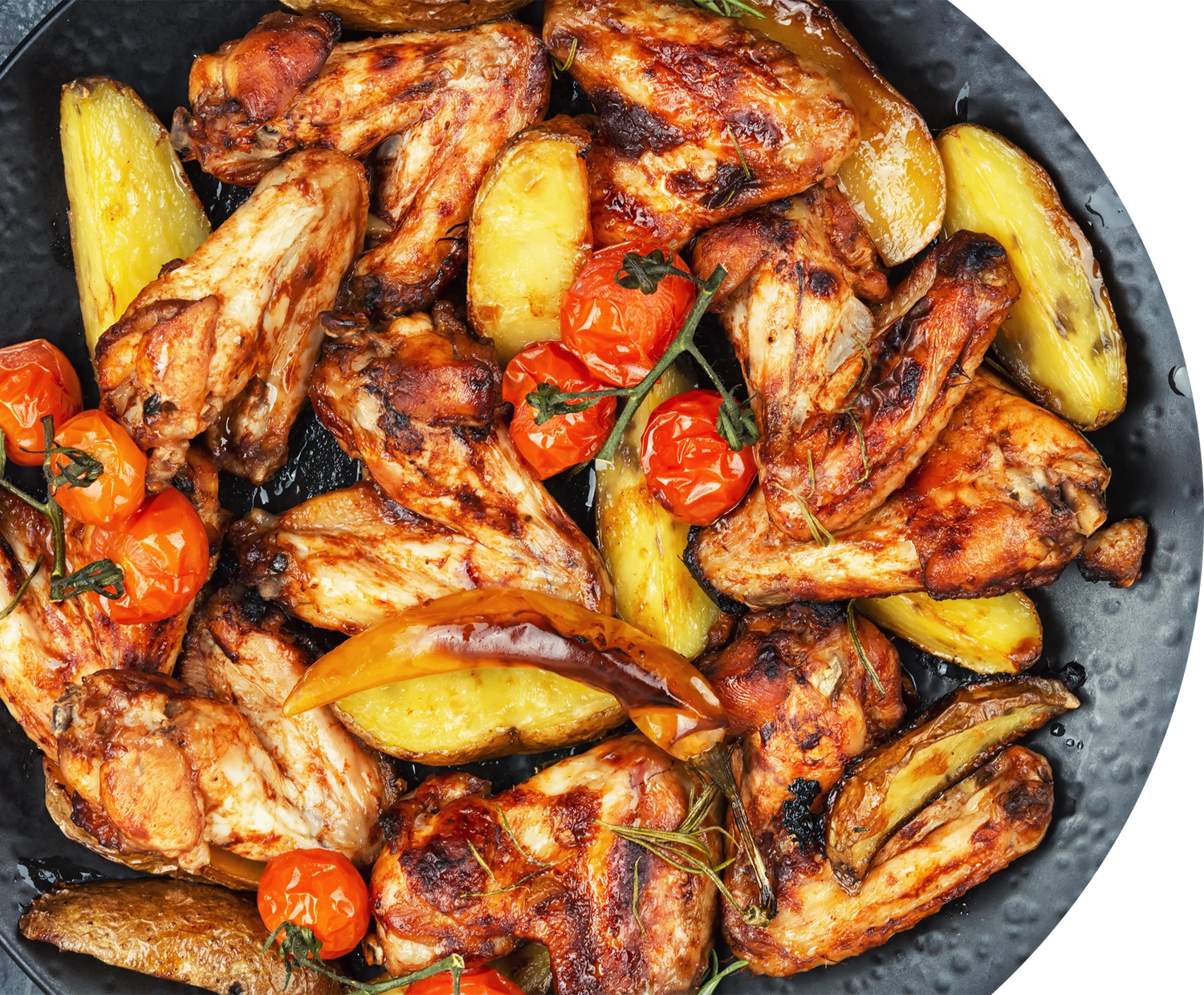 Grilled chicken wings with potatoes and cherry tomatoes on a black plate